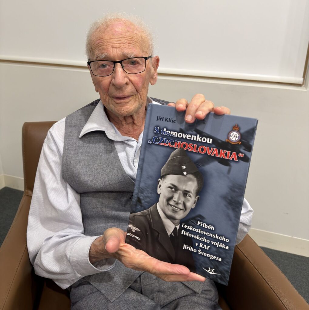 Starý pán sedí v křesle a drží v rukou knihu o svém životě.