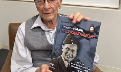 Starý pán sedí v křesle a drží v rukou knihu o svém životě.